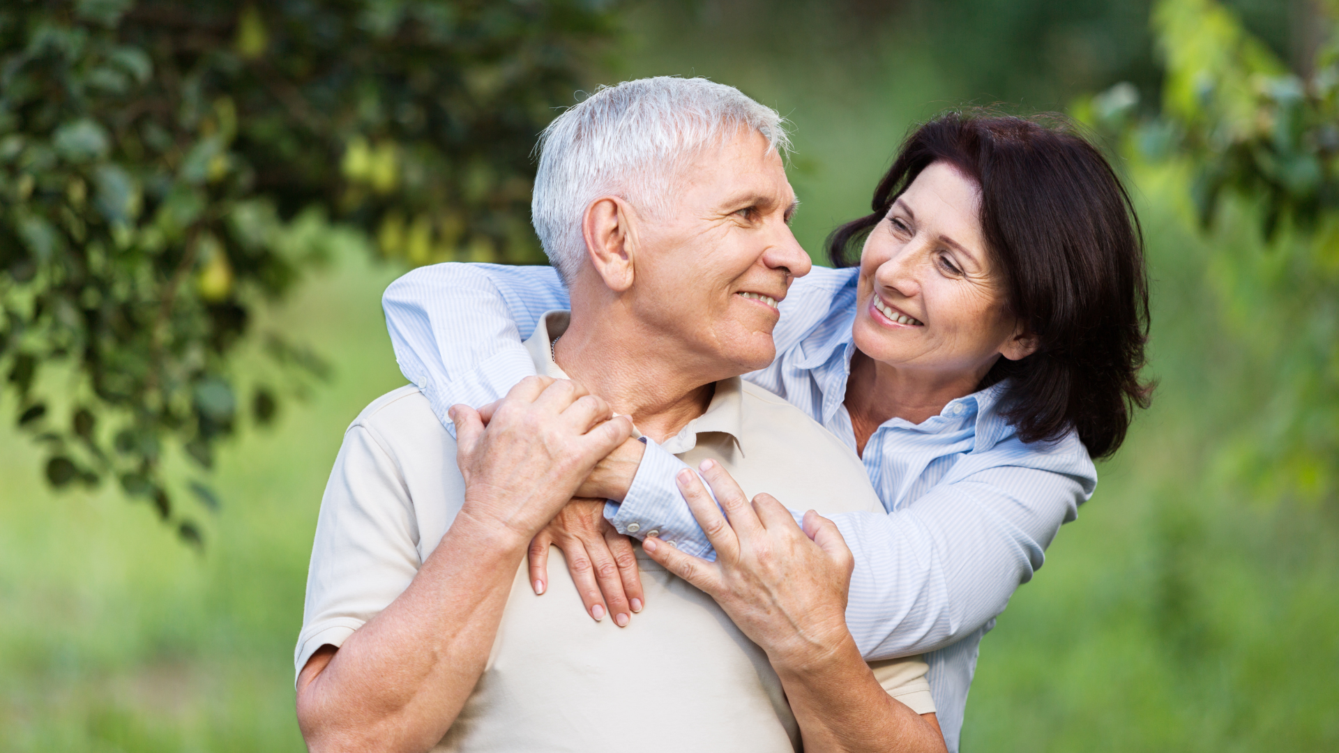 A woman is hugging an older man in a park.
