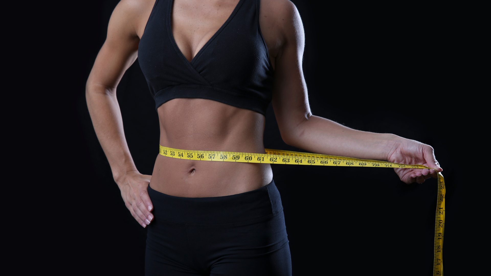 A woman is measuring her waist with a tape measure.