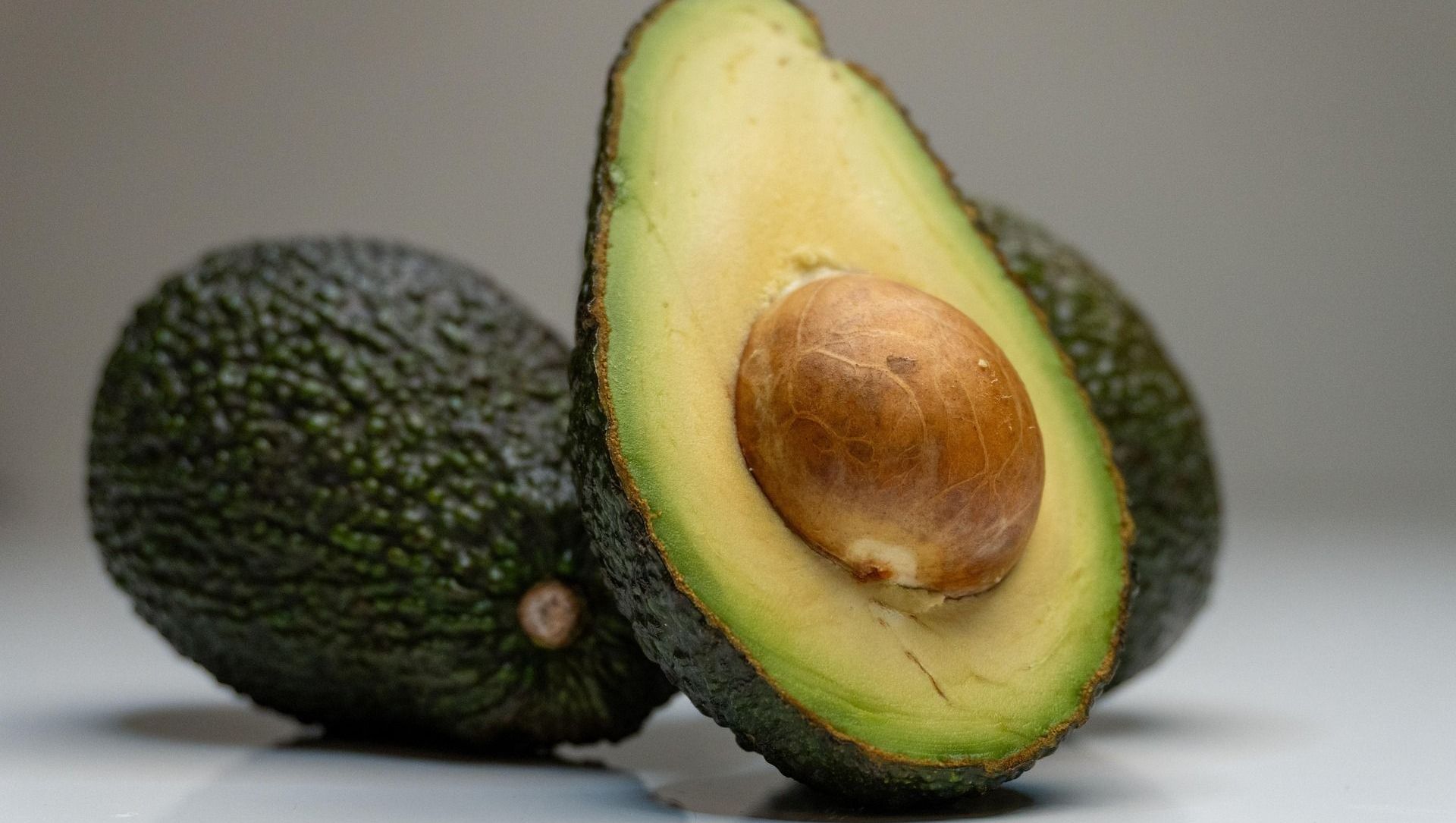 Two avocados are cut in half on a white surface.