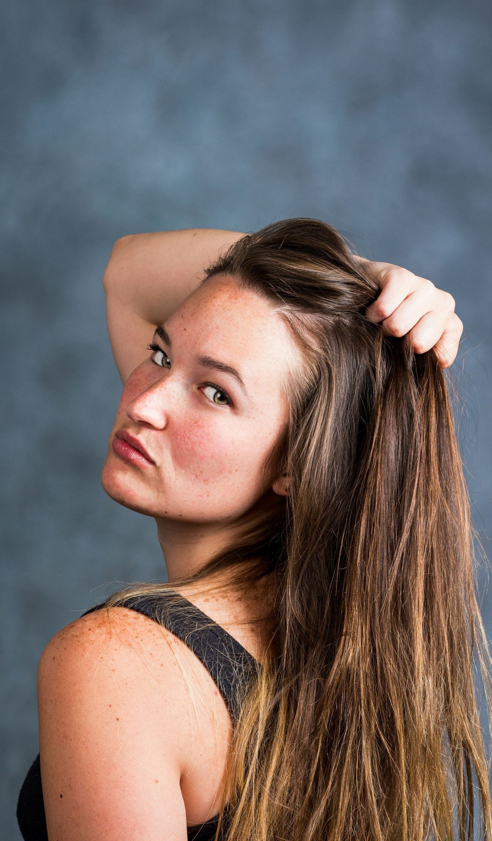A woman with long hair is holding her hair and looking over her shoulder.