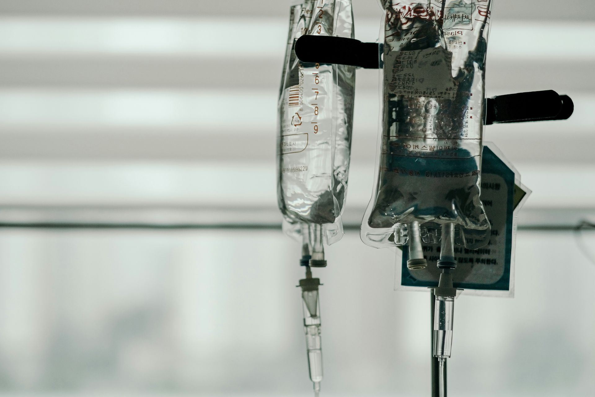 Two bags of liquid are hanging from a pole in a hospital room.