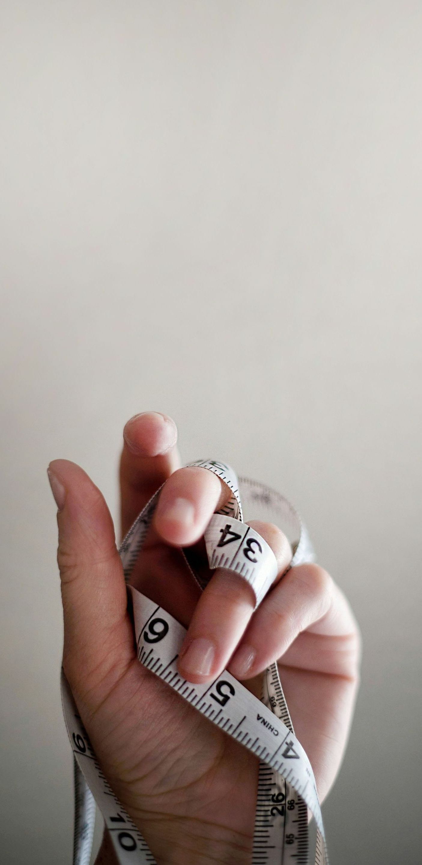 A hand holding a white tape measure with black numbers. The tape measure is wrapped around the fingers.