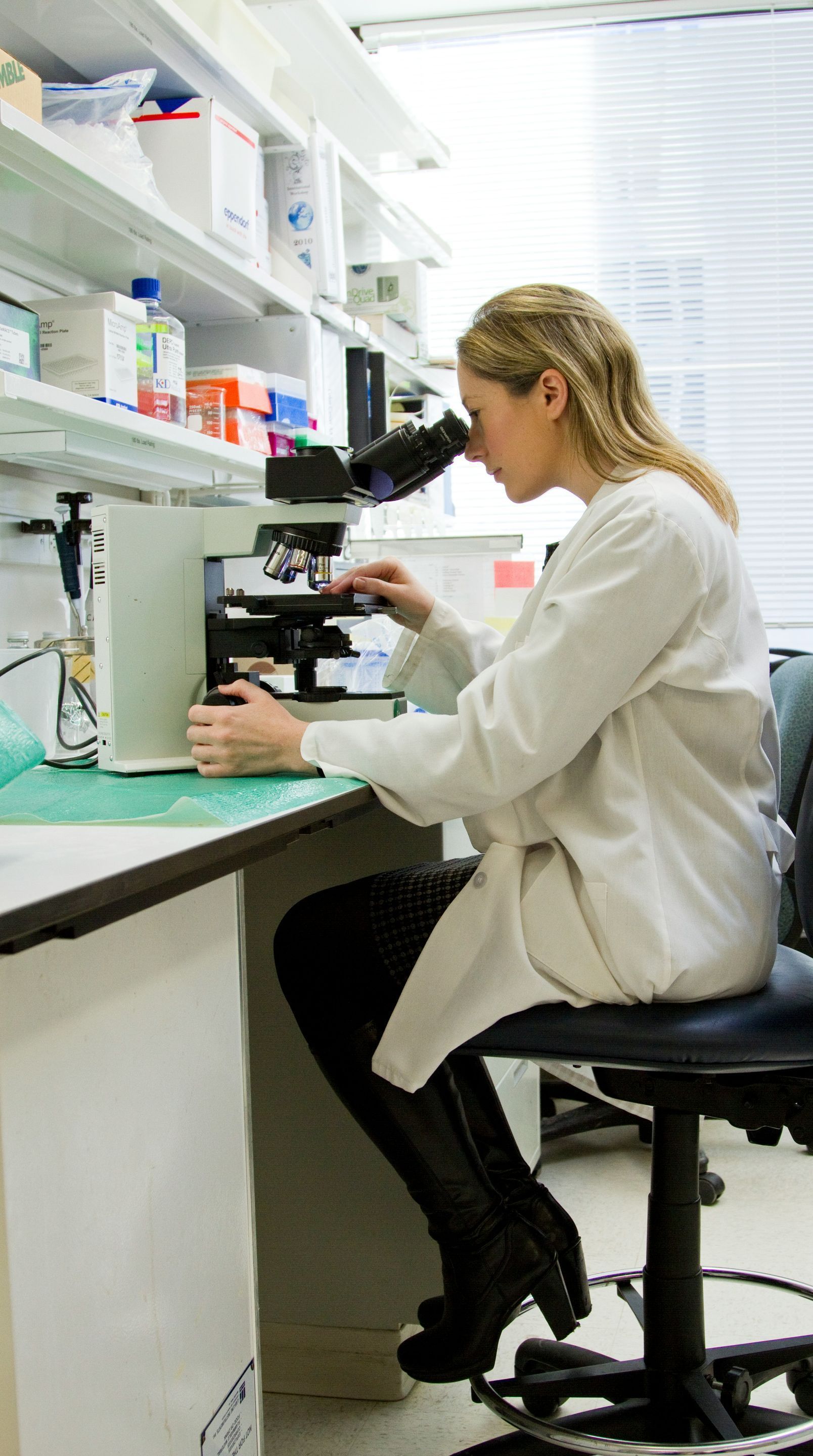 A woman is sitting at a desk looking through a microscope.