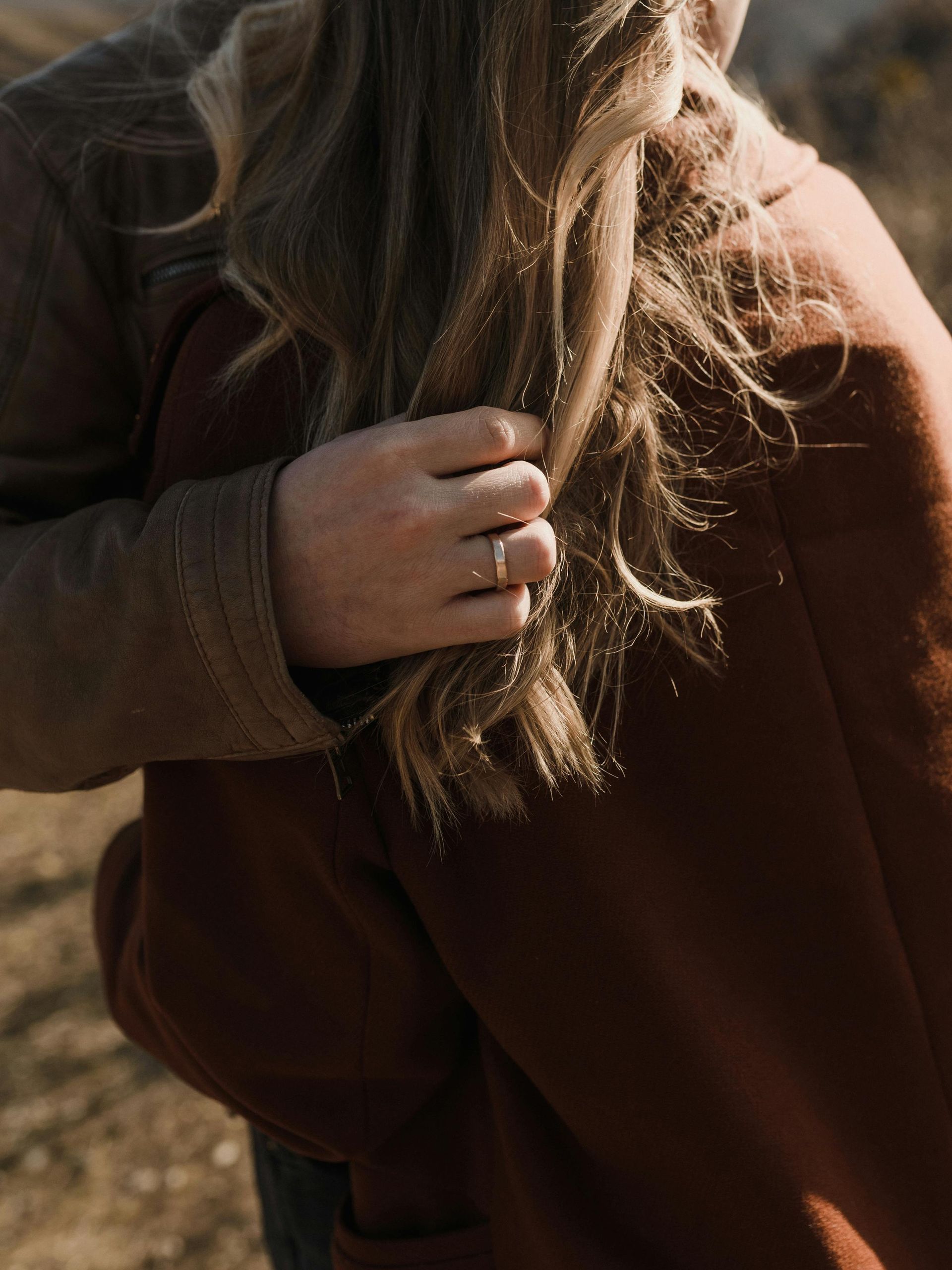 A man is holding a woman 's hair while wearing a ring on his finger.