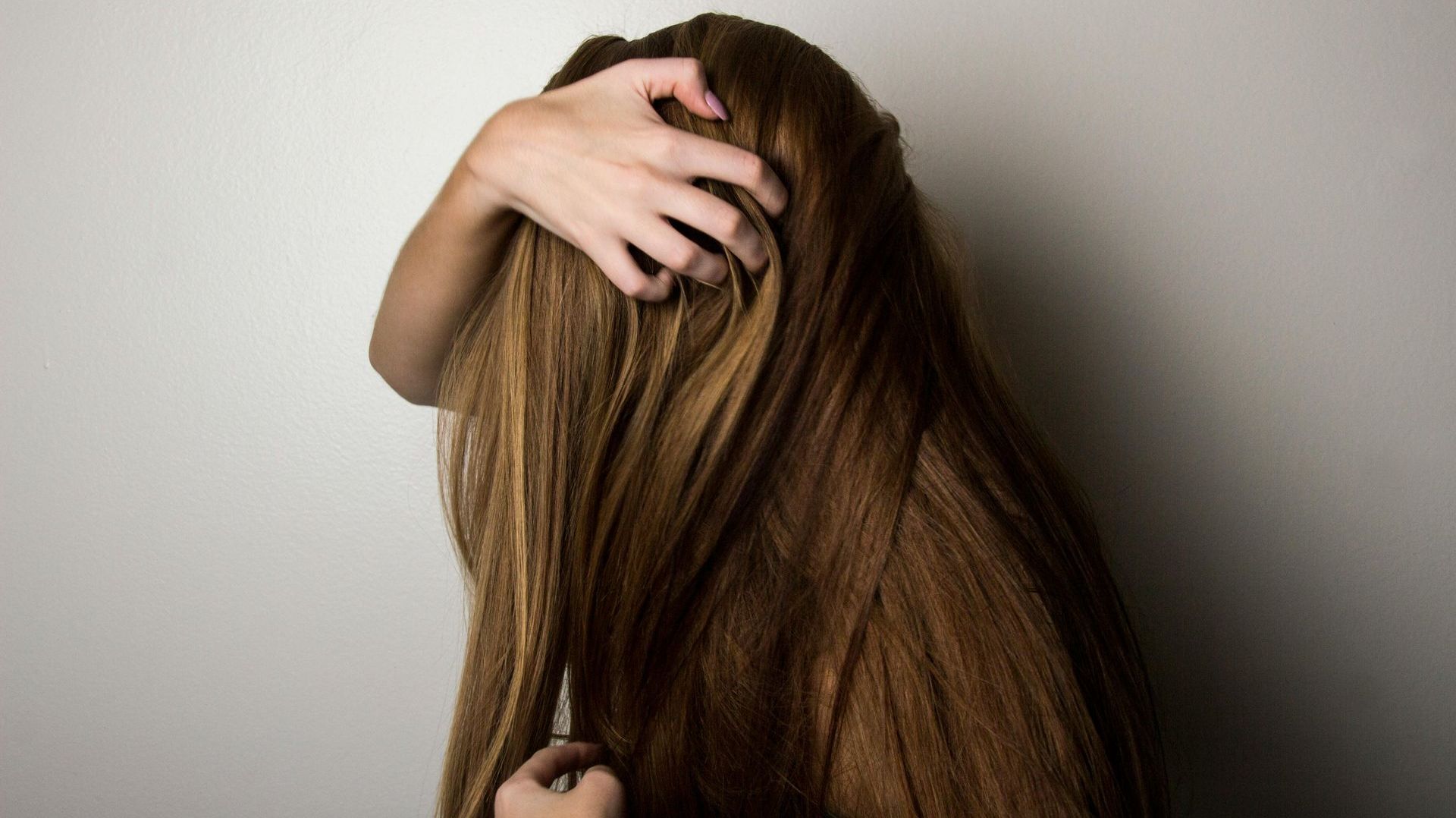 A woman with long brown hair is holding her hair with her hands.