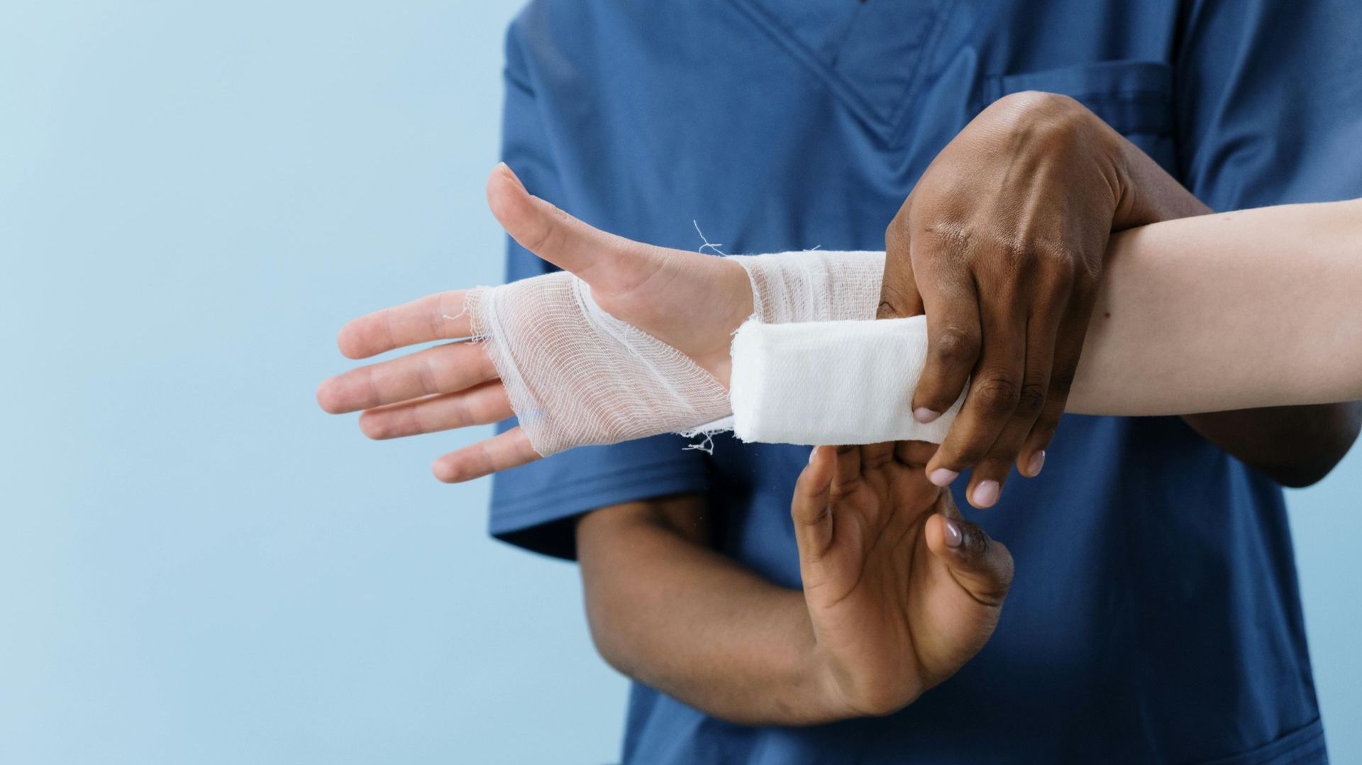 A nurse is wrapping a patient 's wrist with a bandage.