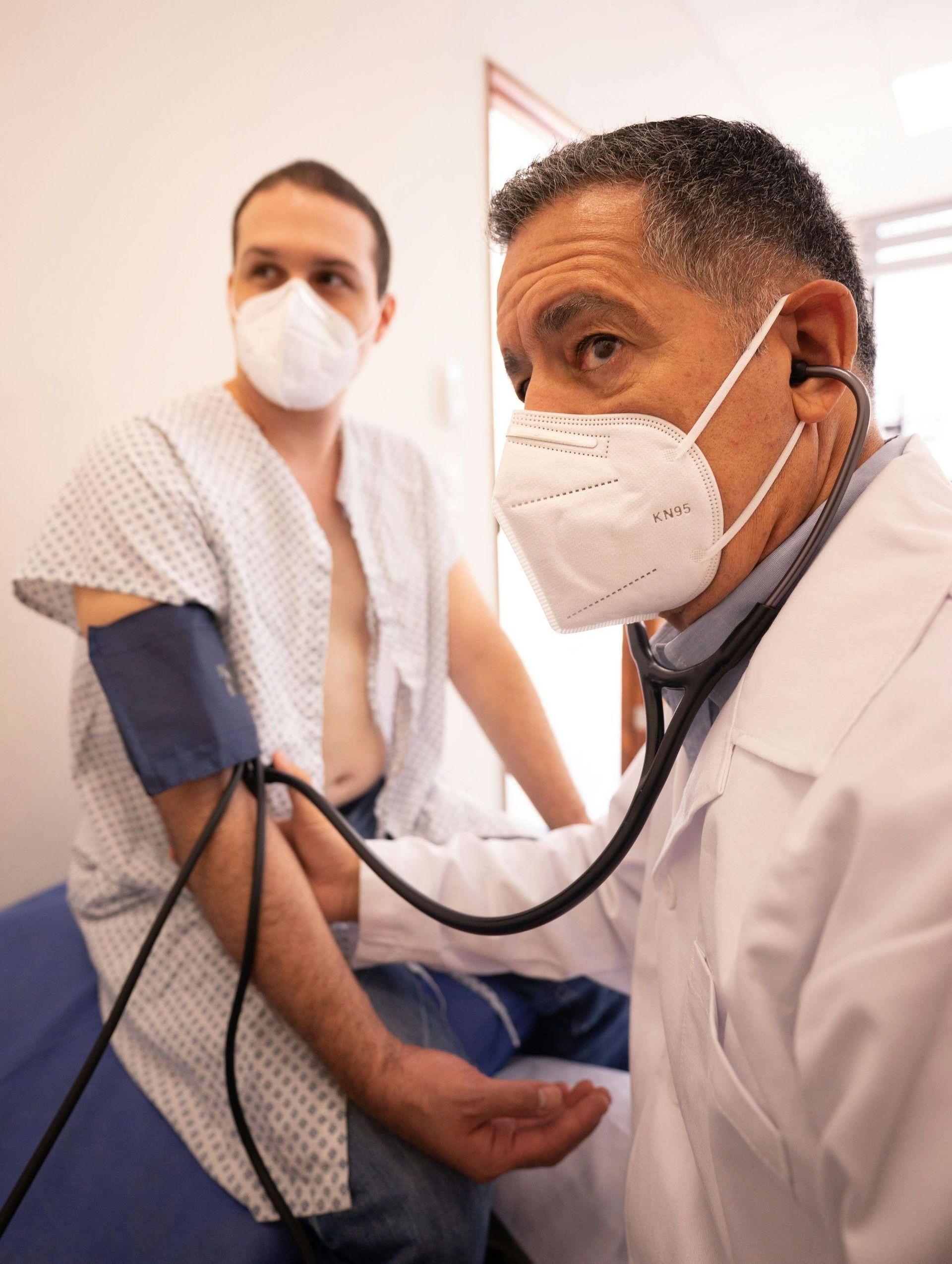 A doctor wearing a mask is listening to a patient 's heartbeat with a stethoscope.