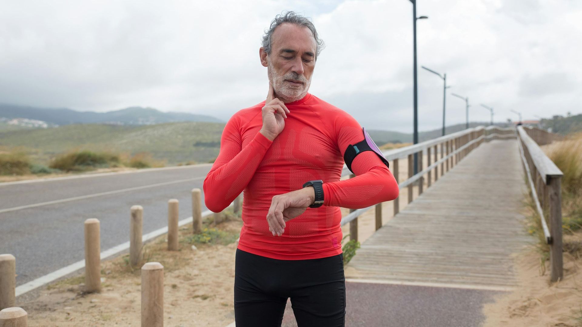 A man in a red shirt is looking at his watch.