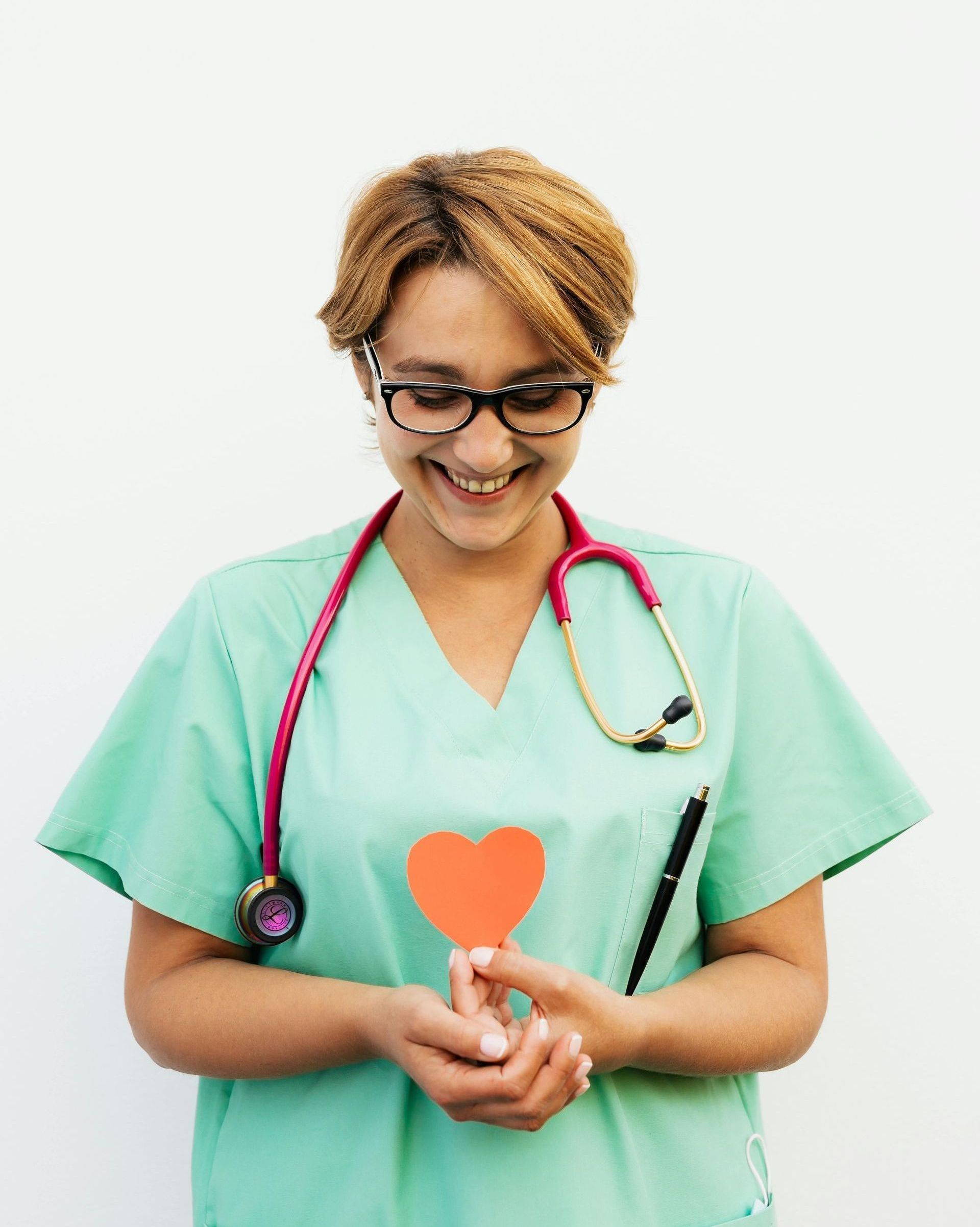 A nurse with a stethoscope around her neck is holding a red heart in her hands.
