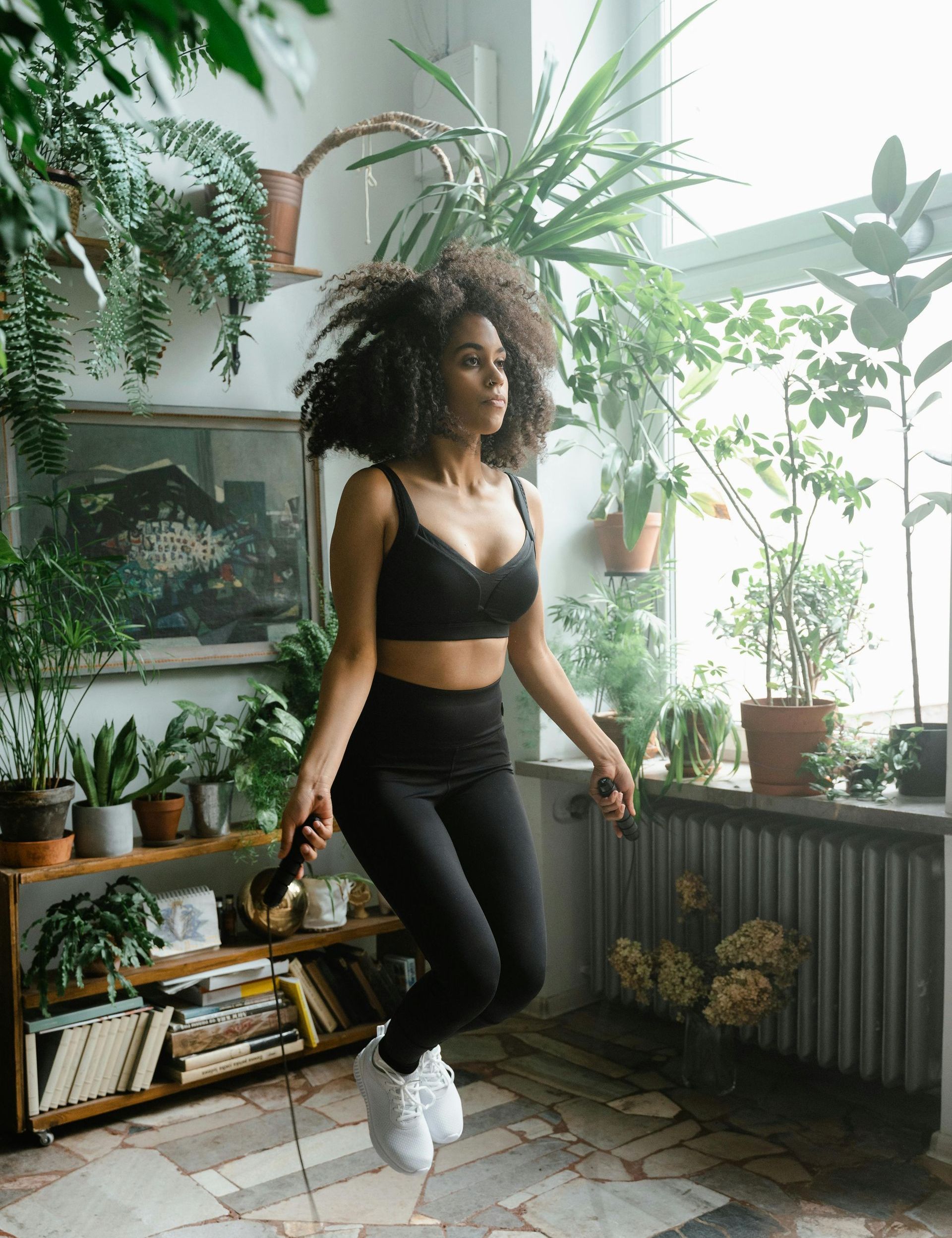 A woman is jumping a jump rope in a room filled with plants.
