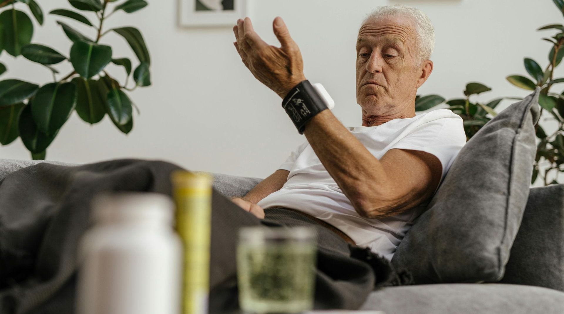 An elderly man is sitting on a couch taking a pill.