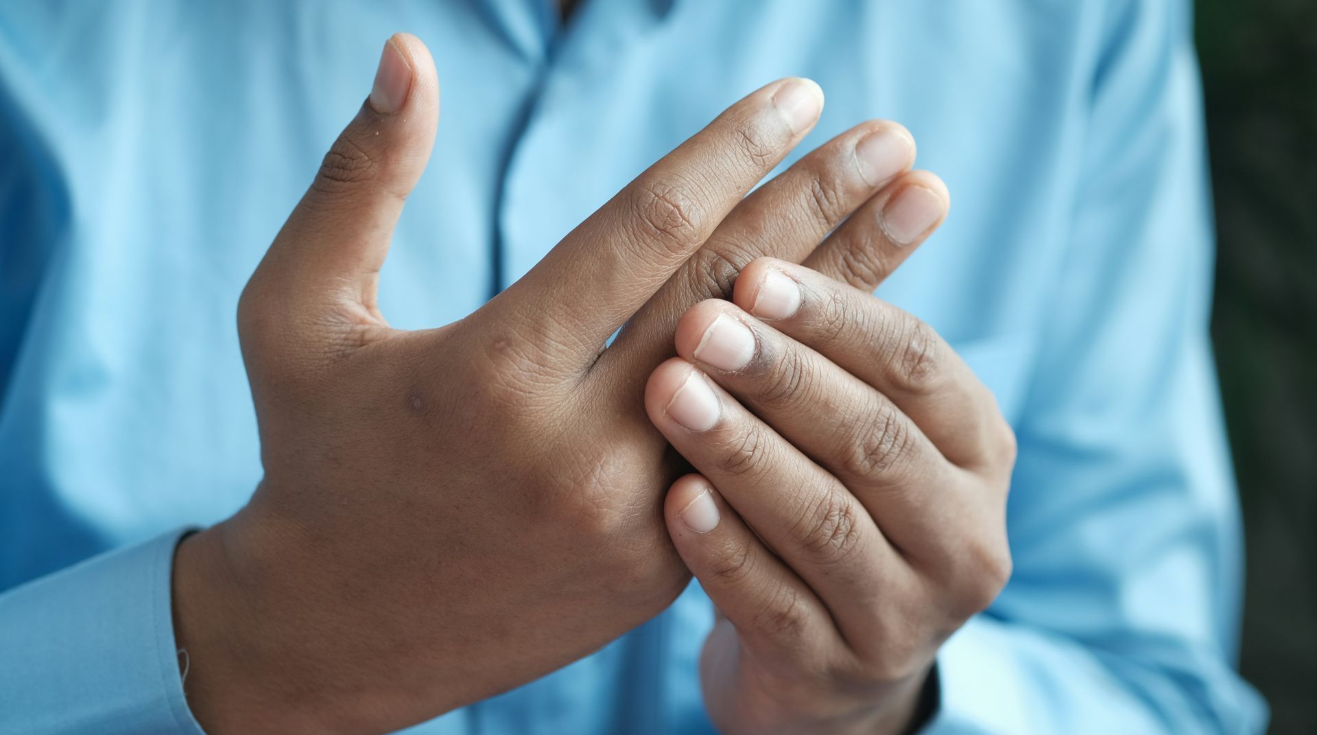A man in a blue shirt is holding his hand in pain.