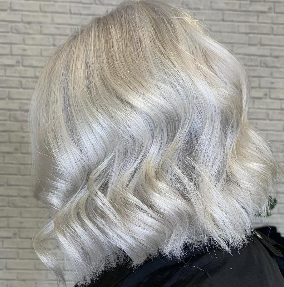 A Woman with Blonde Hair Is Standing in Front of A White Brick Wall — Eden Hair in Pacific Paradise, QLD