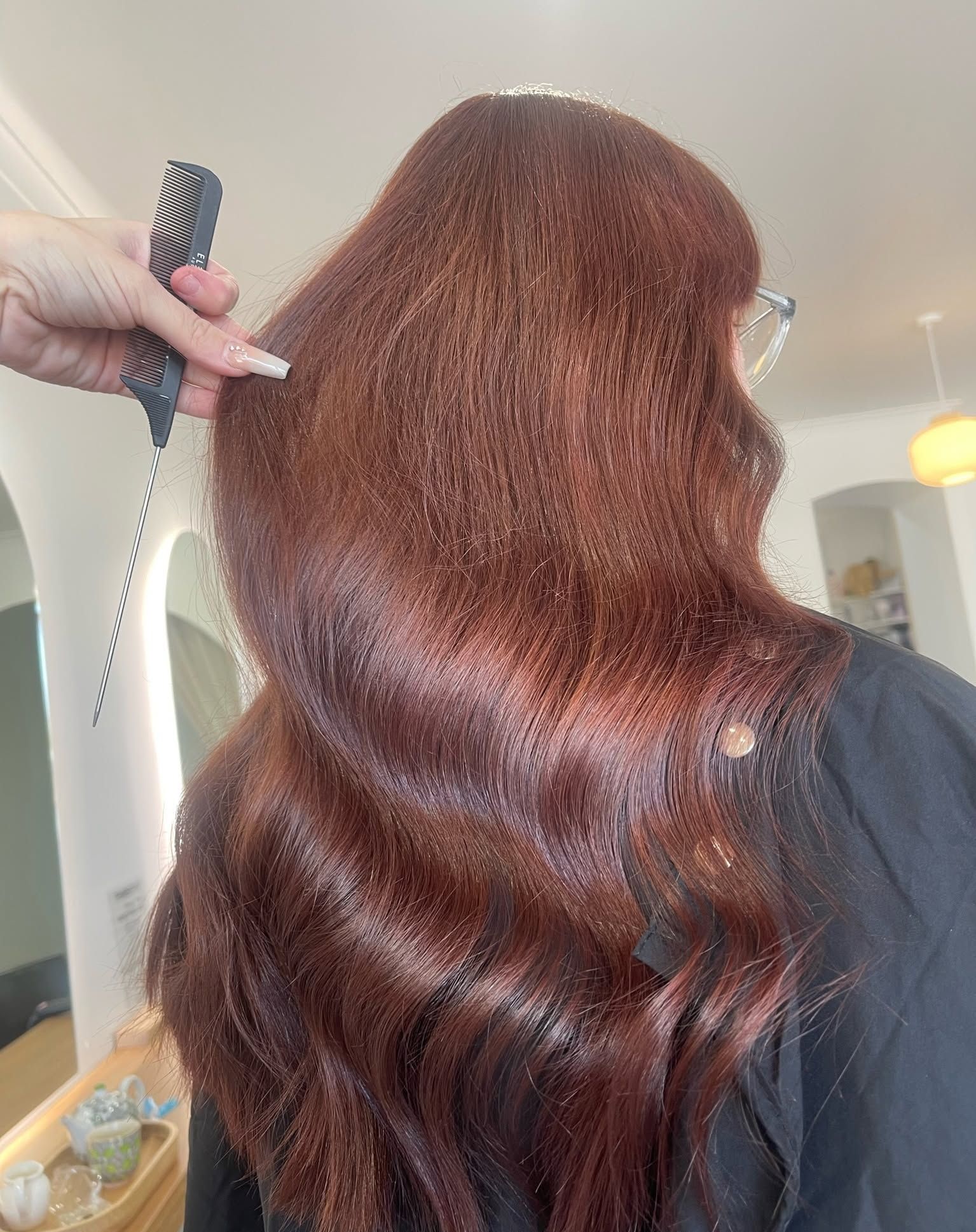 Person with long, wavy auburn hair being combed in a salon — Eden Hair in Pacific Paradise, QLD