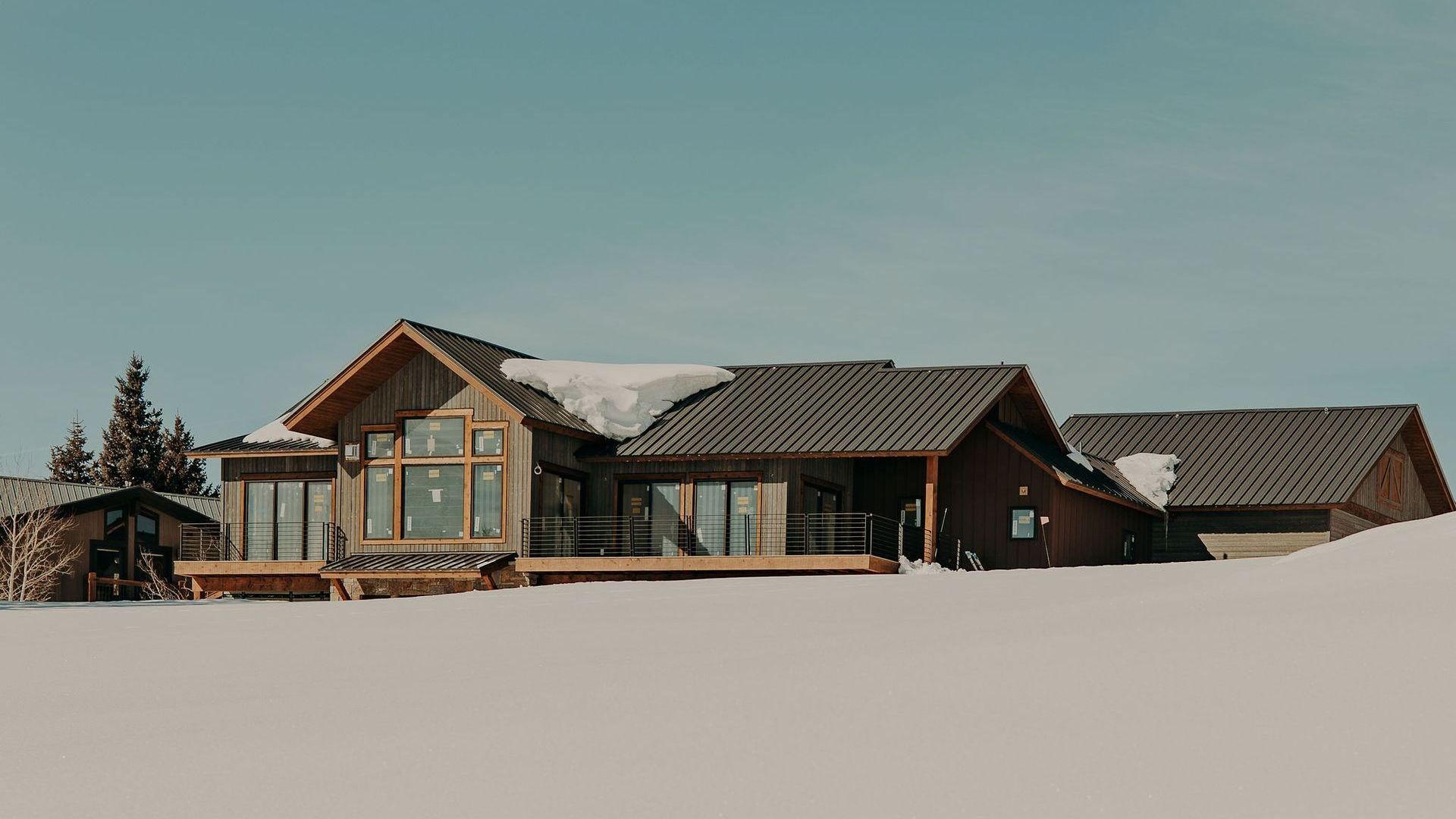 A large wooden house is sitting in the middle of a snow covered field.