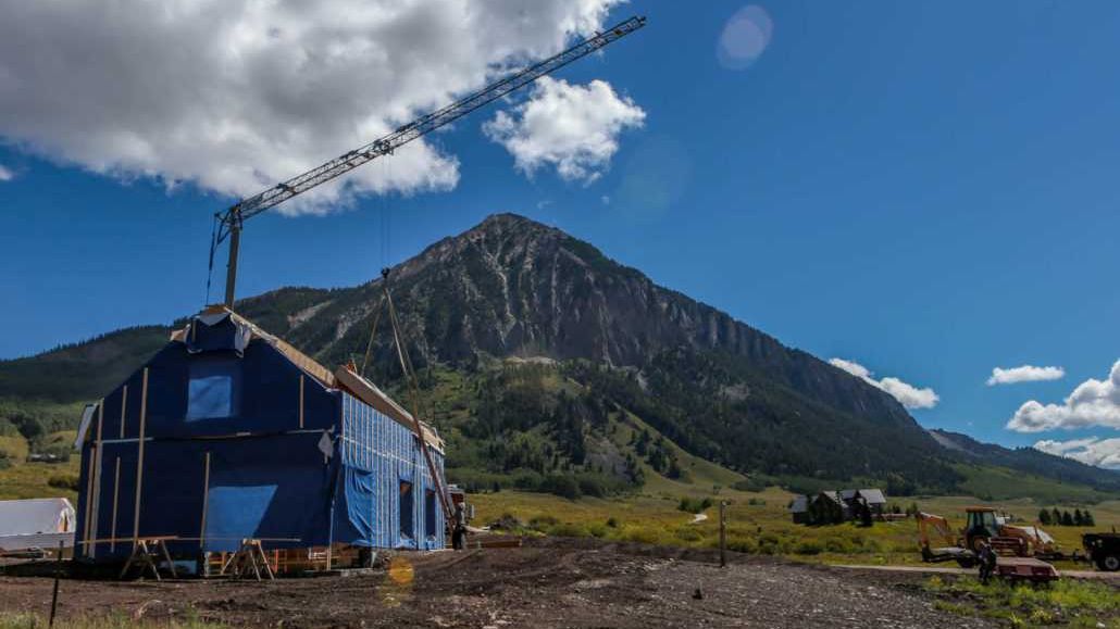 A house is being built in the mountains with a crane in the background.