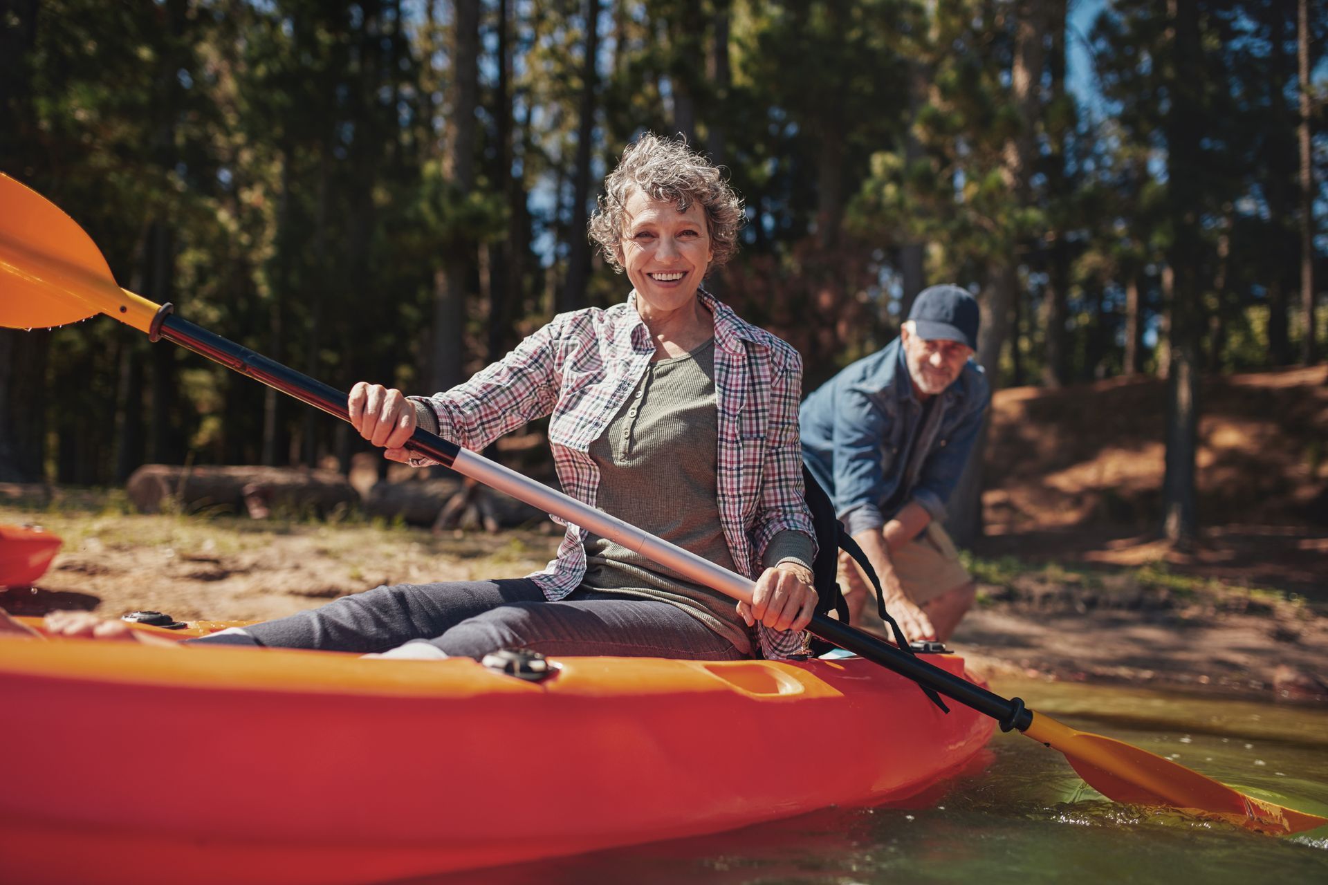 Two people paddling a red kayak on a calm lake with trees in the background