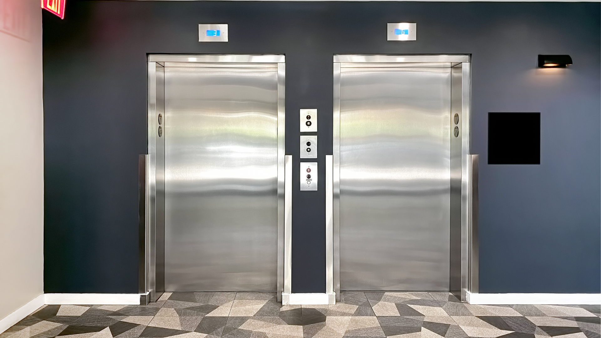 Two stainless steel elevator doors in a dark blue hallway. Up/down buttons are present.