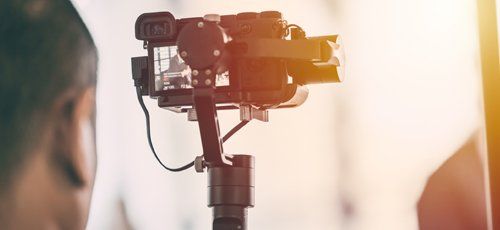 A person filming with a camera attached to a handheld gimbal in front of a bright light.