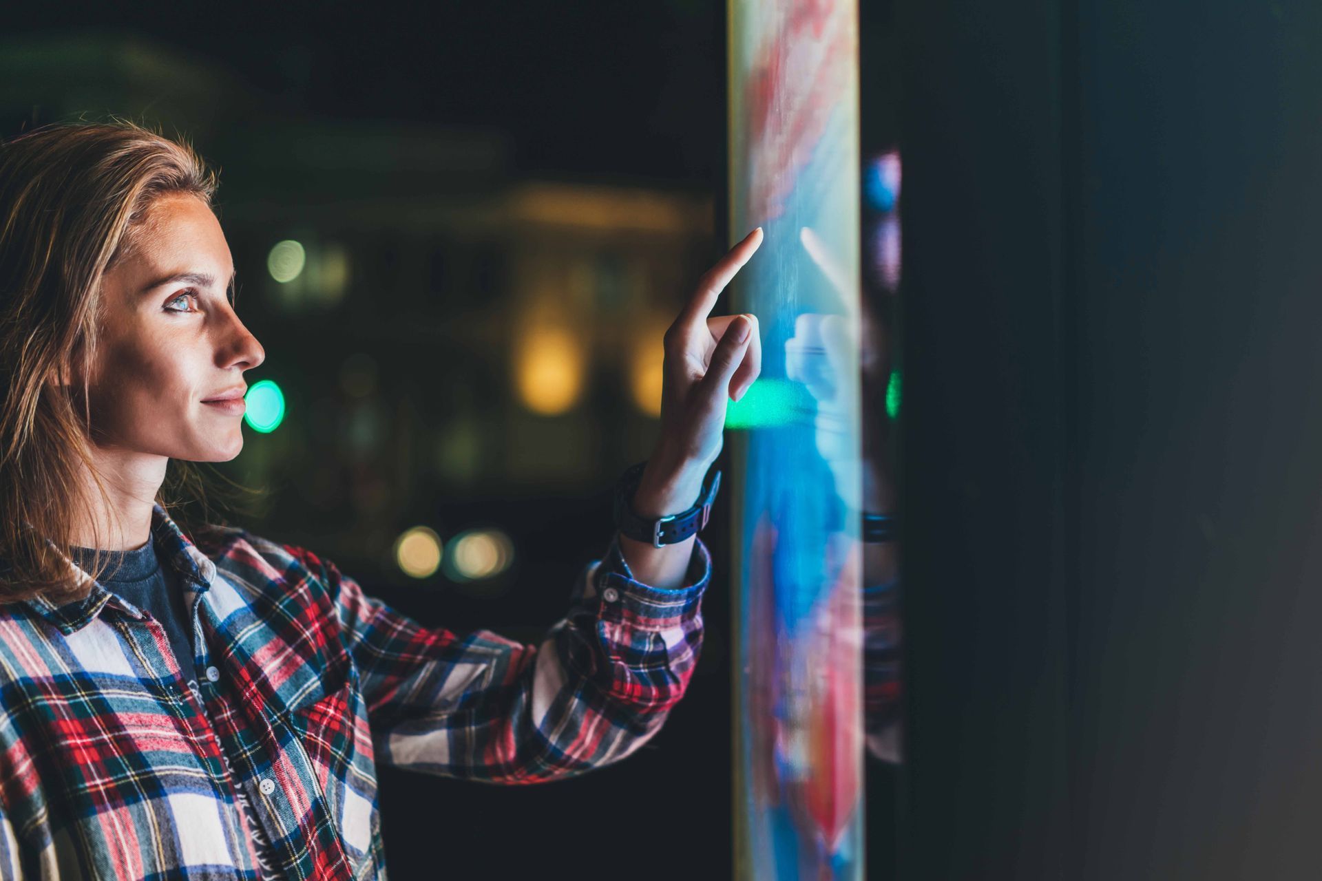 Woman using an interactive flat panel display with vibrant digital graphics at night.