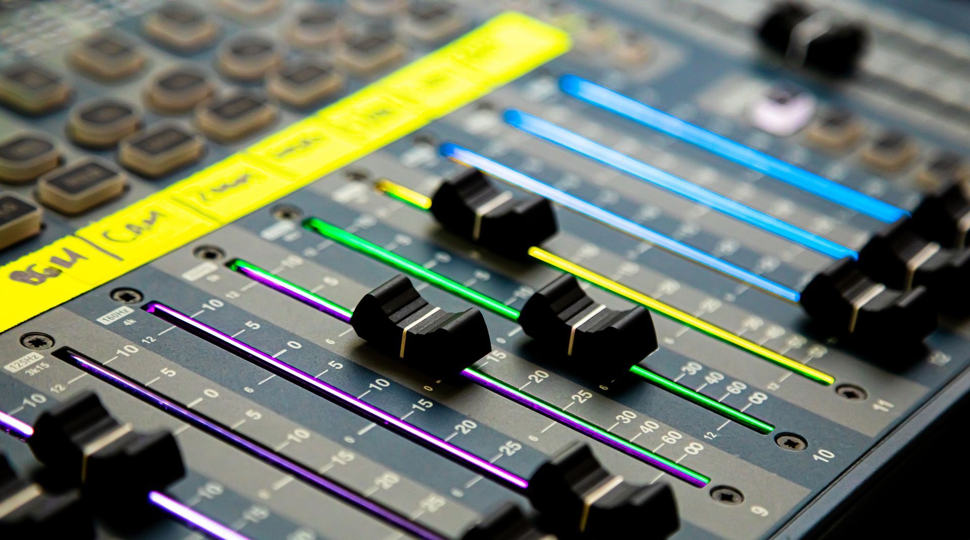 Close-up of sound mixing console with colorful faders and labeled controls.