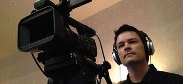 A man operating a professional video camera while wearing headphones during filming.