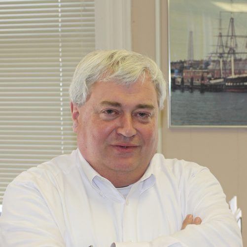 A man with his arms crossed in front of a picture of a ship