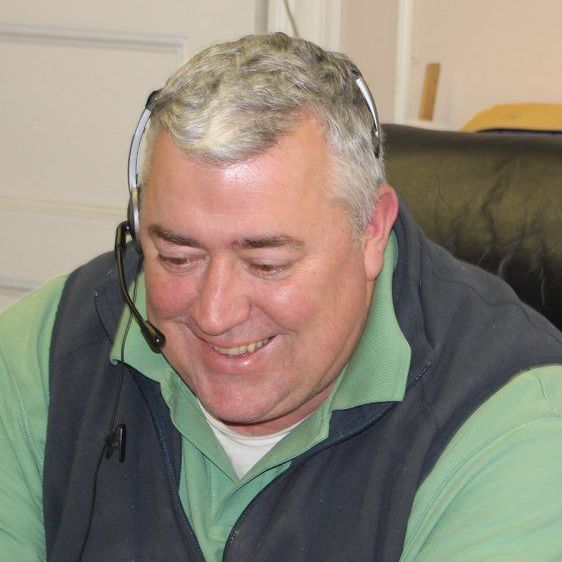 A man wearing a headset is smiling while sitting in a chair