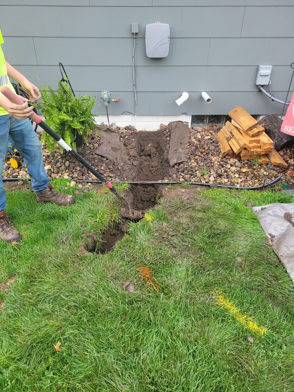 Person digging trench in grass next to house, with dirt pile and markings.