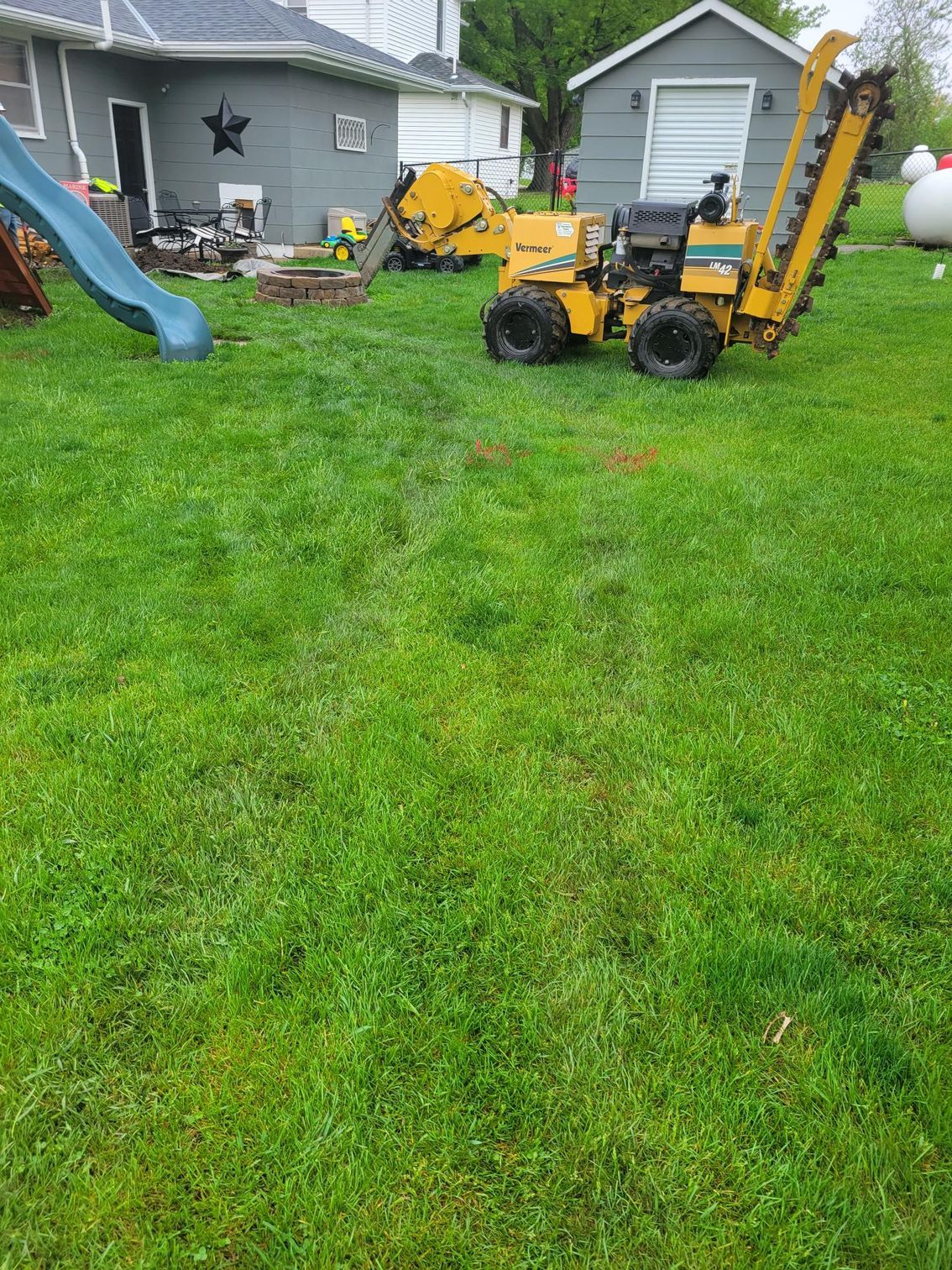 A trenching machine on a grassy lawn near a house and a slide.