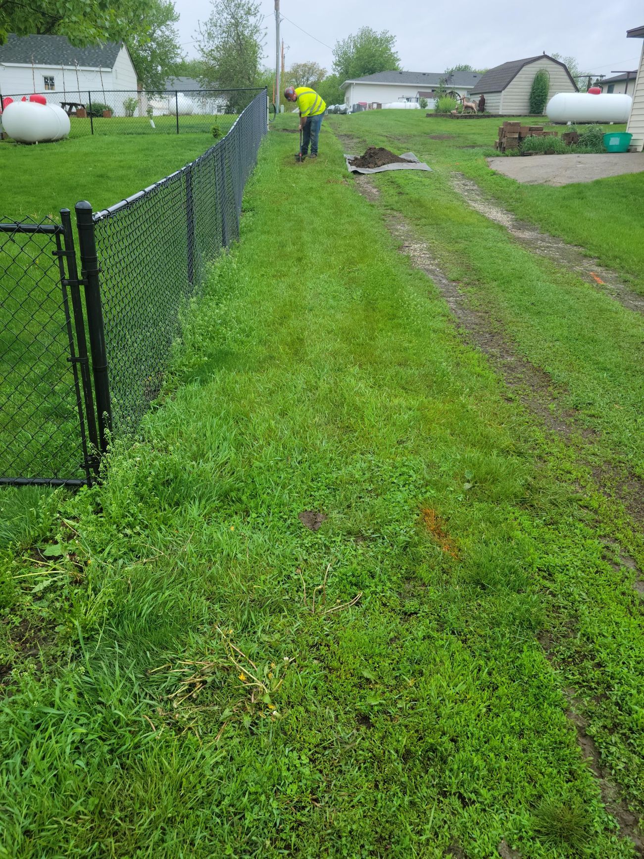 Person in safety vest working in grassy yard next to a black chain link fence.