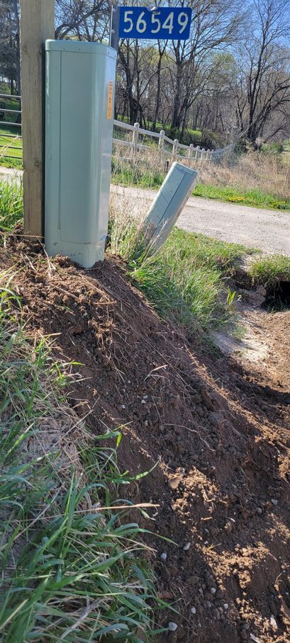 Utility pole with box, address sign (56549), and soil along roadside.