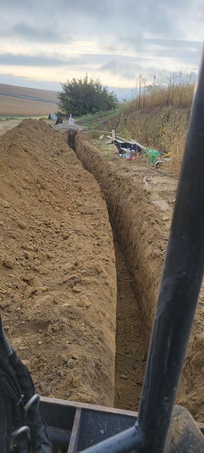 A trench has been dug in a field. Brown soil, cloudy sky. From a machine's perspective.