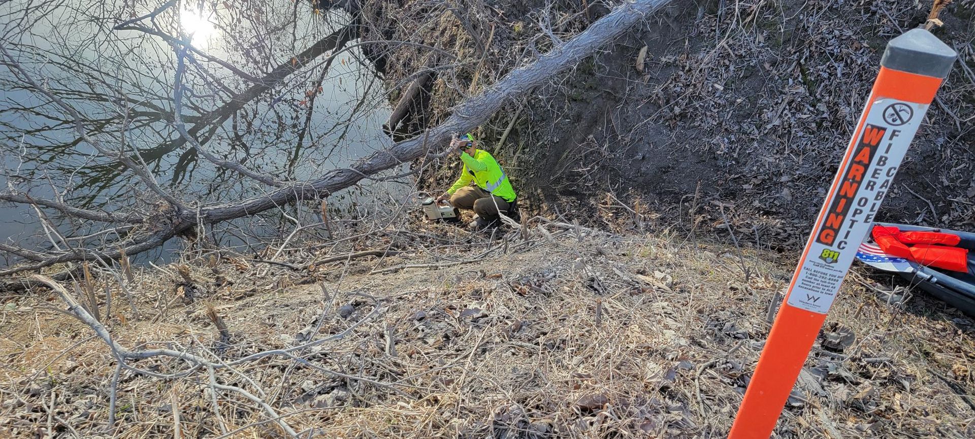 Person in a neon vest near a body of water. An orange marker is in the foreground.
