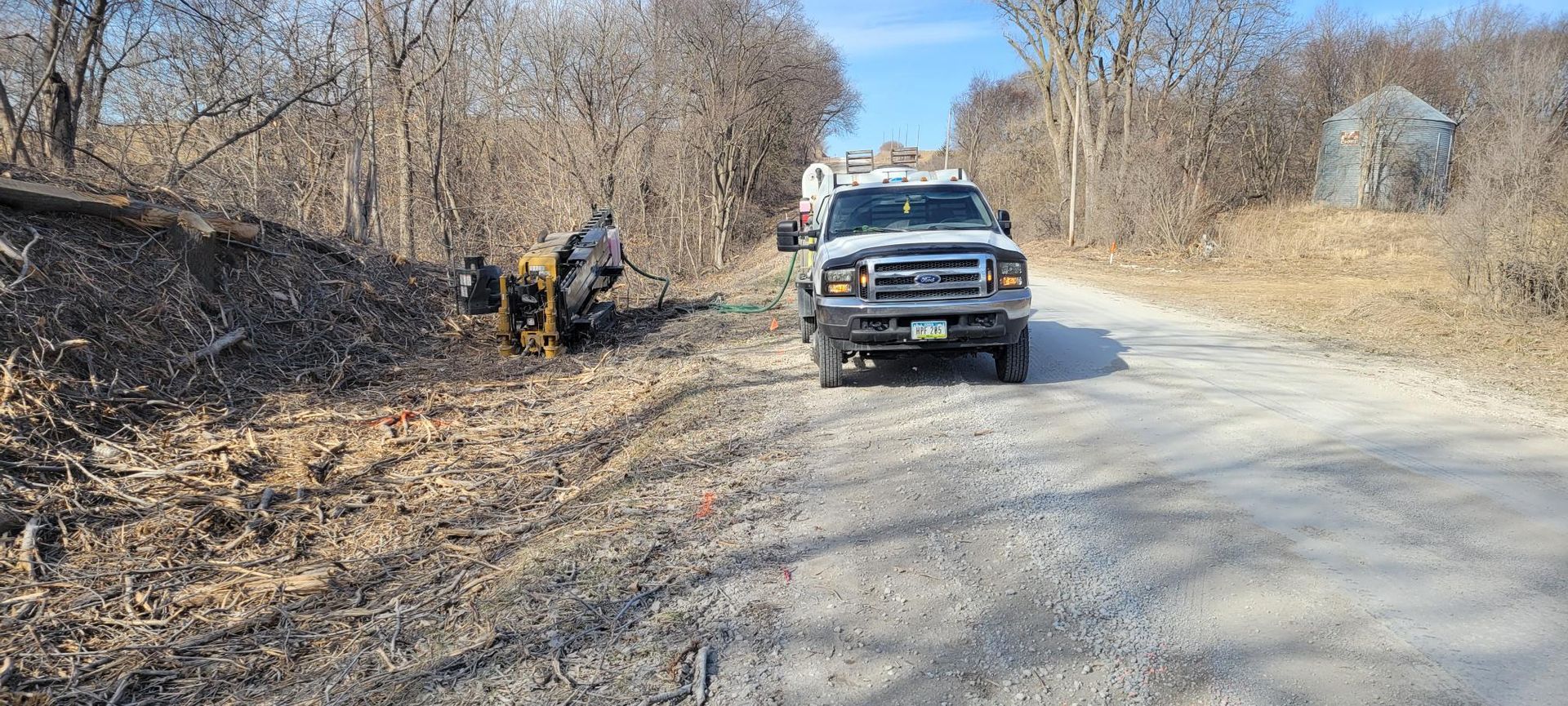 A truck on a gravel road, construction work underway on the side of the road, and trees lining the road.