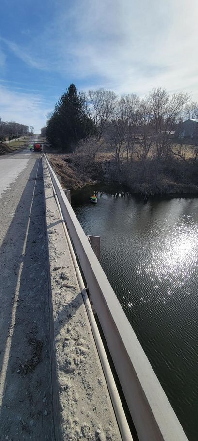 Bridge over water on a sunny day. Road, trees, and sky visible.