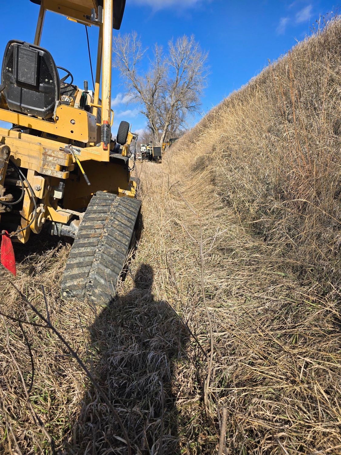 Yellow bulldozer on a steep, dry, grassy hill. Clear blue sky.