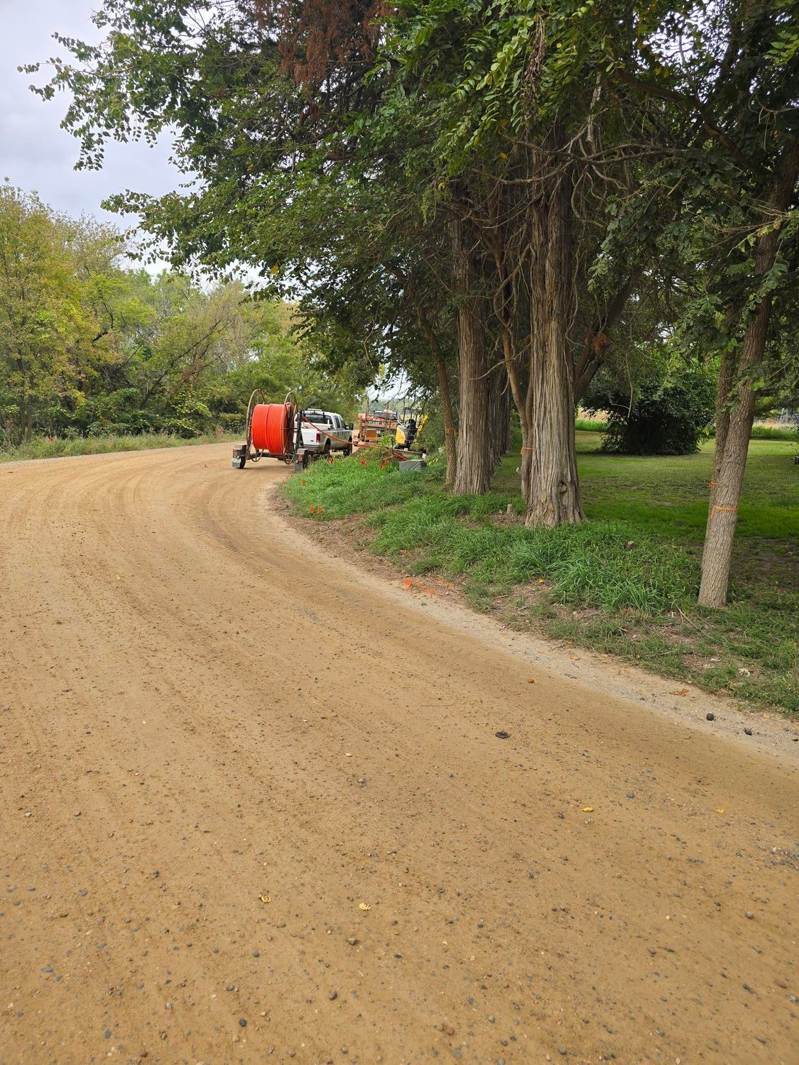 Dirt road curves through trees, a truck and equipment parked ahead.