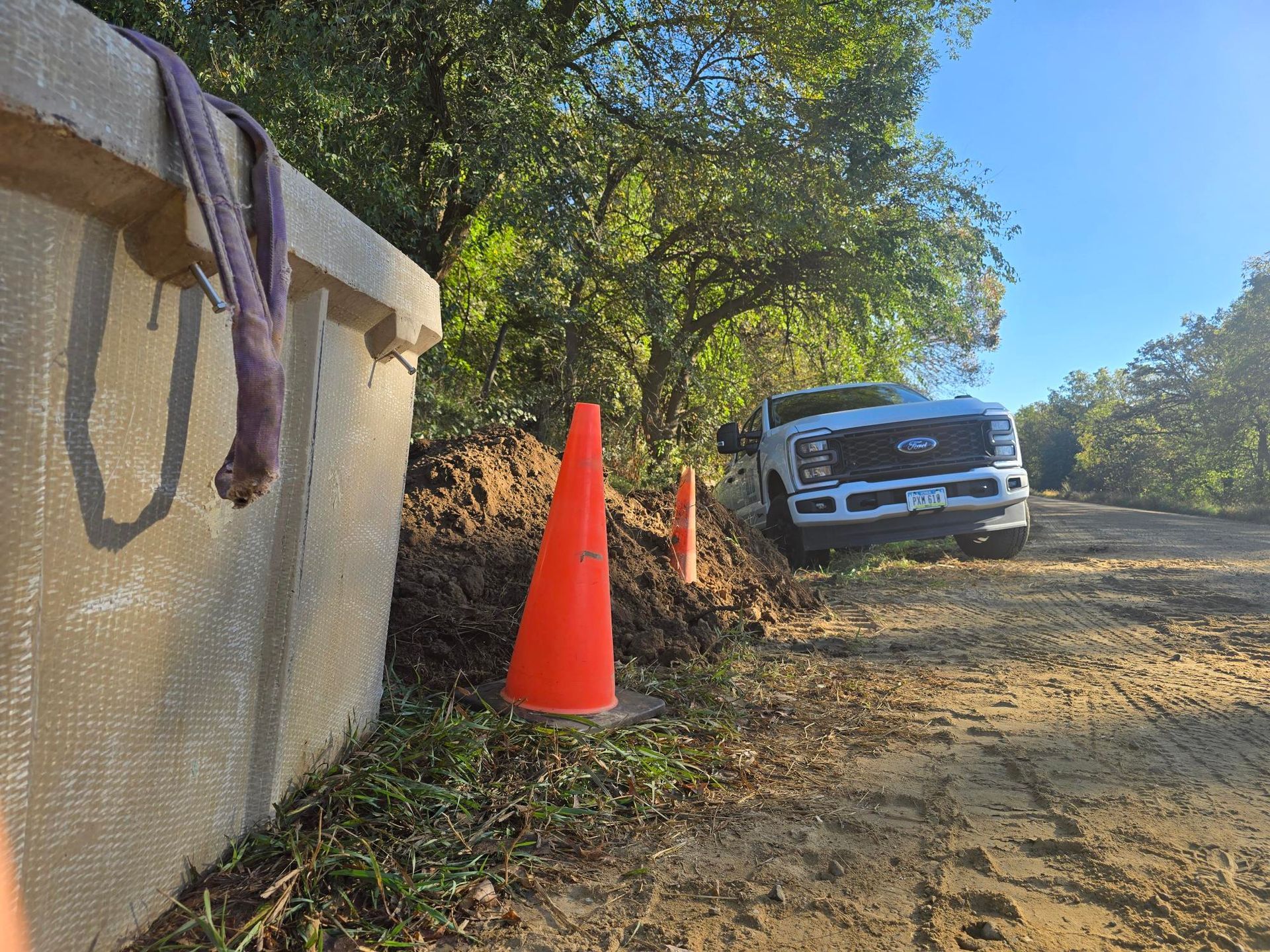 Construction scene: white truck, orange cones, dirt pile, and concrete wall; outdoors on sunny day.