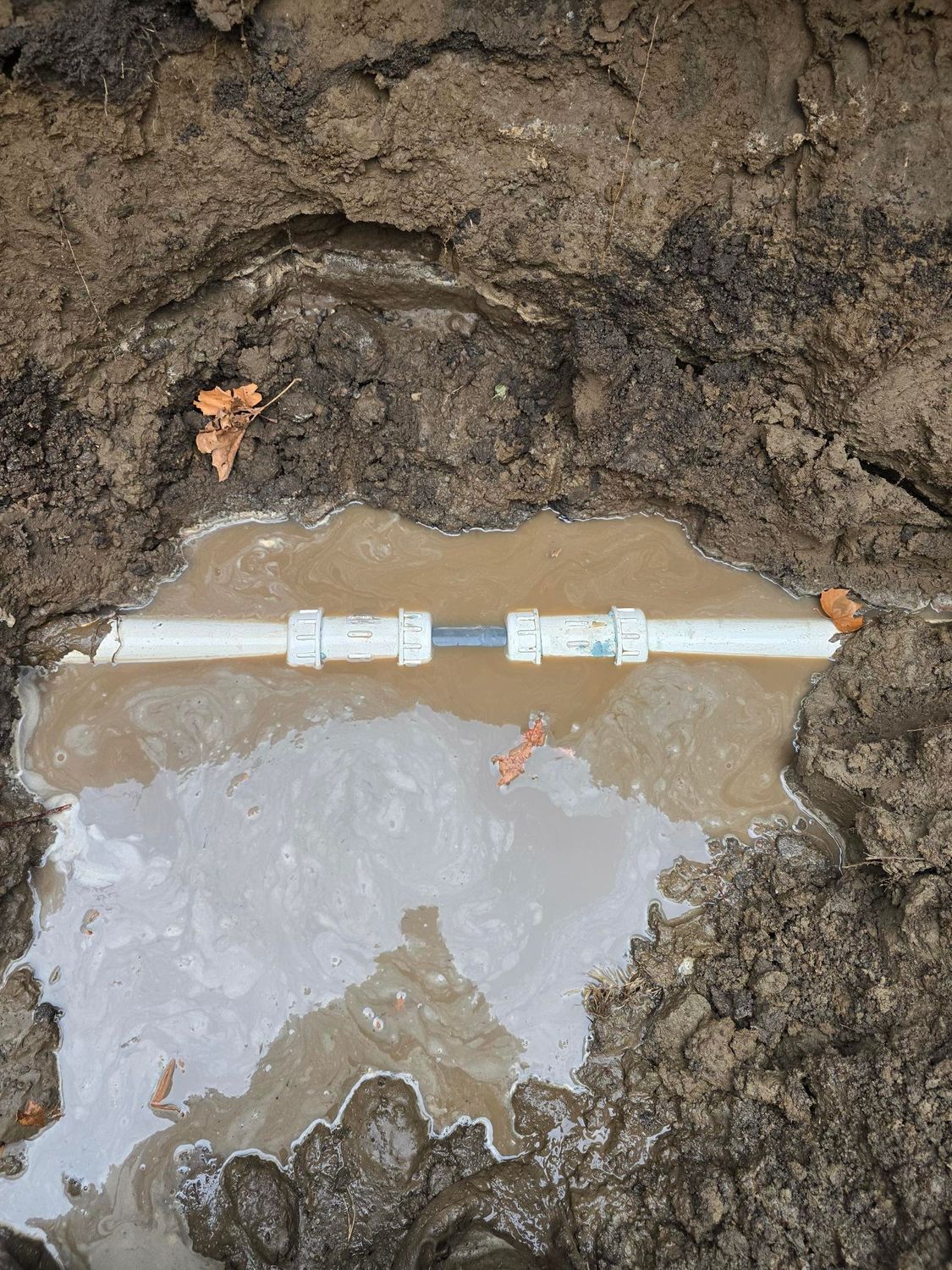 Pipes leaking water in a muddy outdoor setting.