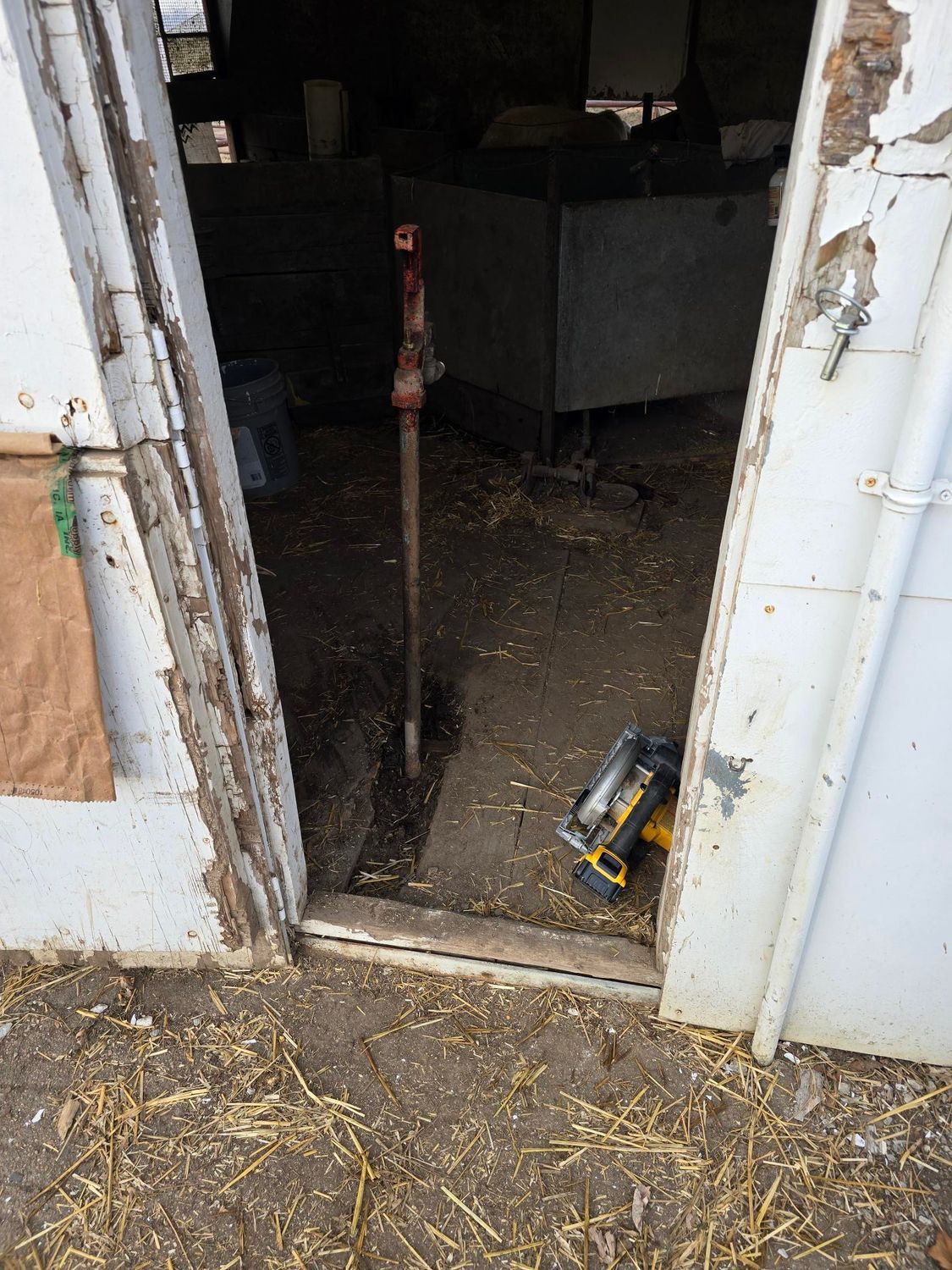 Open doorway of a barn with a jackhammer inside and straw on the floor.