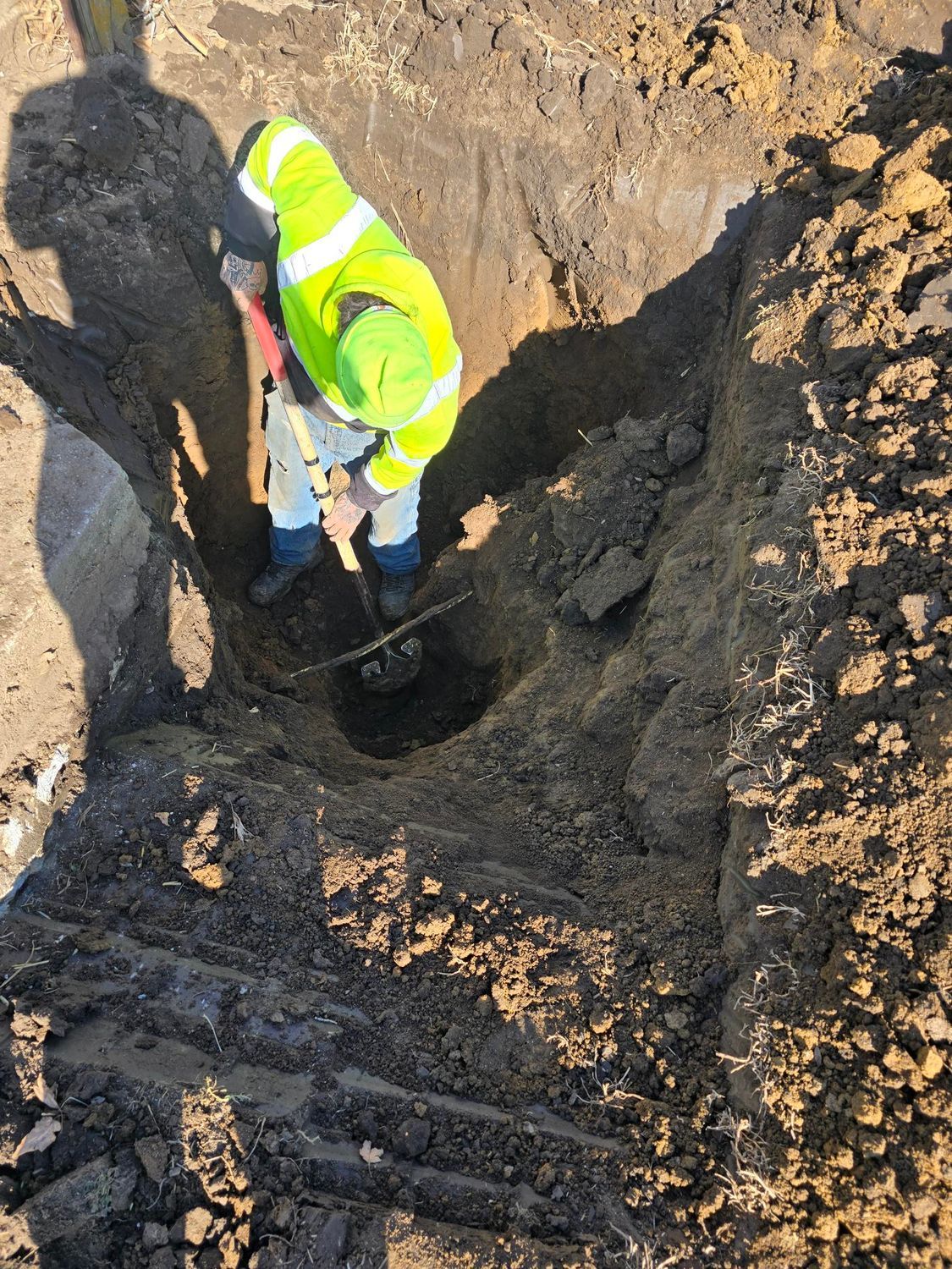 Worker in neon green vest and hard hat digging in a dirt pit.