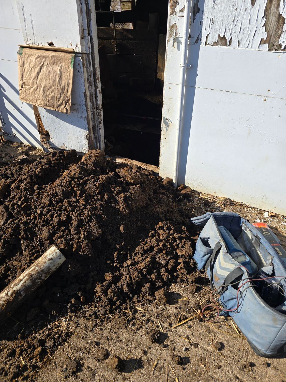 Pile of dirt blocking a doorway of a light blue building; a bag and pipe are nearby.