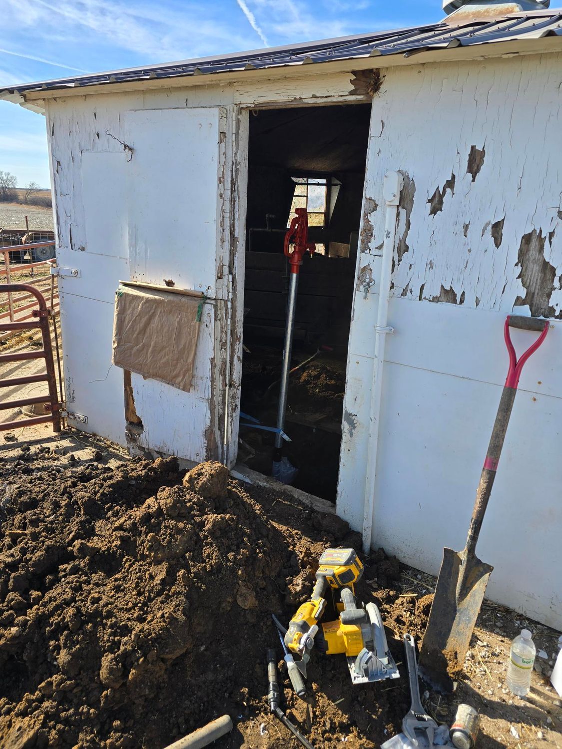 Shed with open door and tools nearby, surrounded by dirt. Exterior has peeling paint.