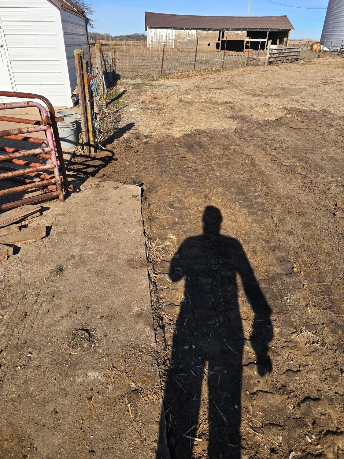 Shadow of a person on dirt path with barn and shed in background.