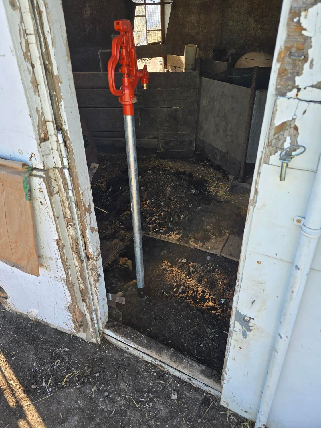 Red water pump inside an open doorway of a dilapidated building.