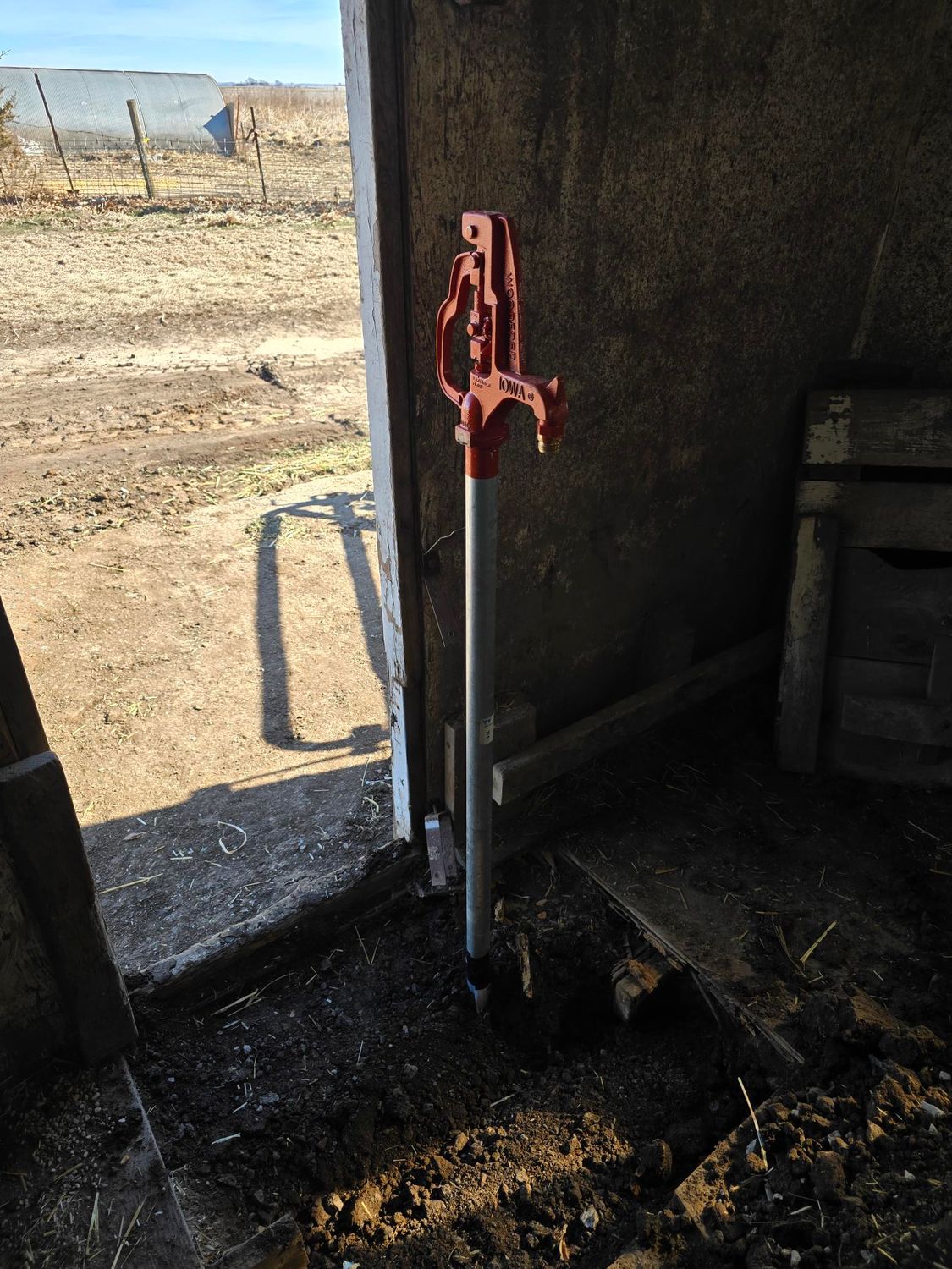 Red handle water pump in a barn doorway.