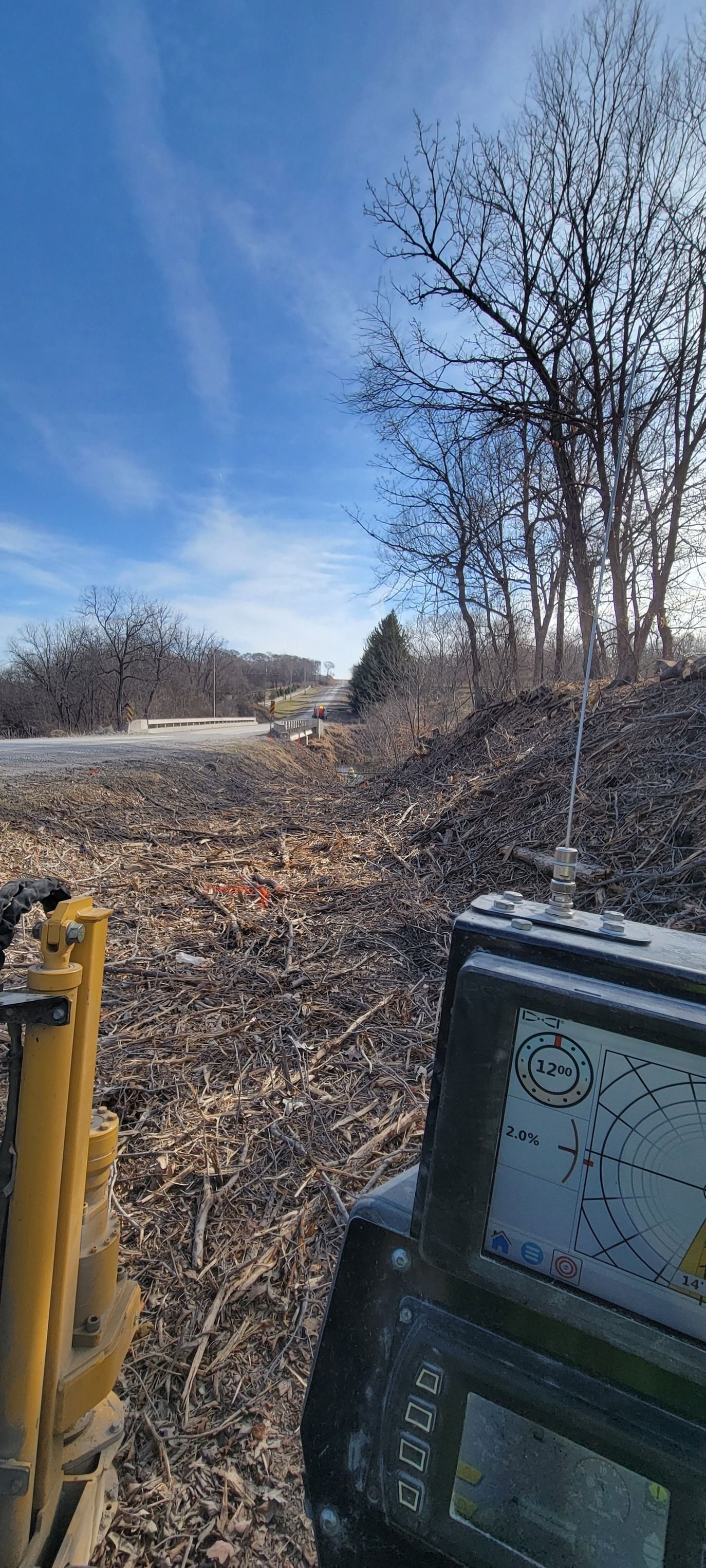 A machine in a field of debris, trees, and a bright blue sky.