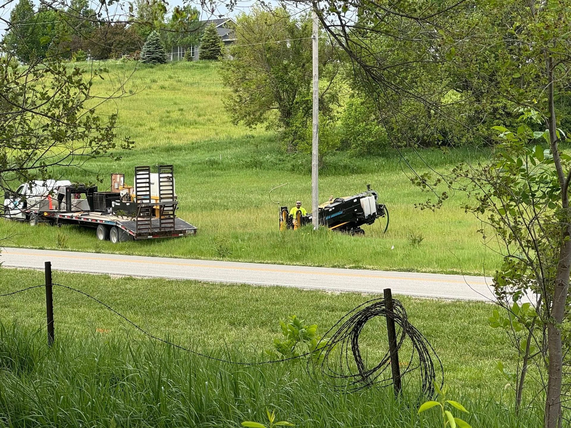 Tractor-trailer and overturned vehicle on a grassy roadside next to a road, with workers present.