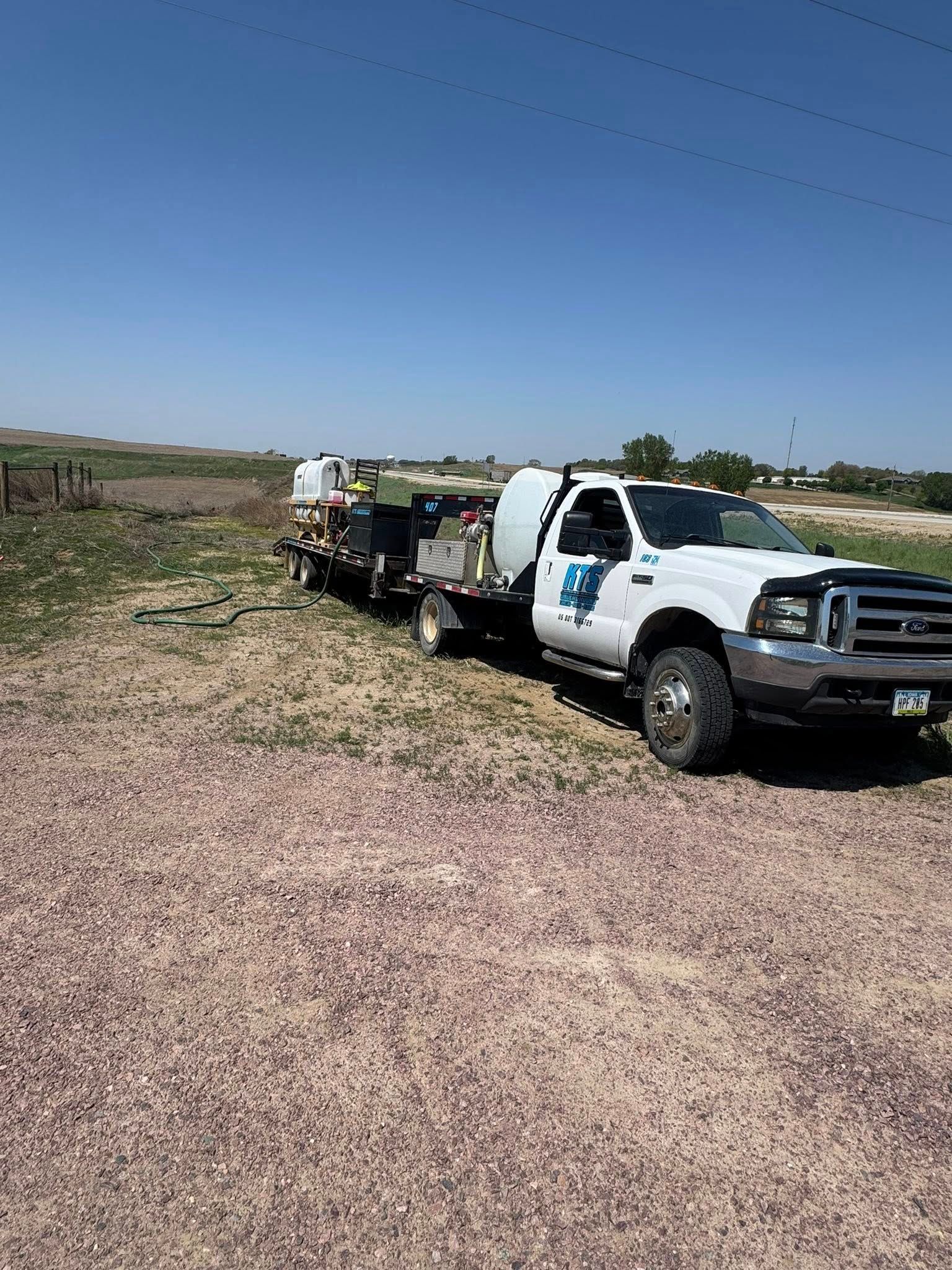 White truck pulling a trailer with tanks on a gravel surface under a blue sky.
